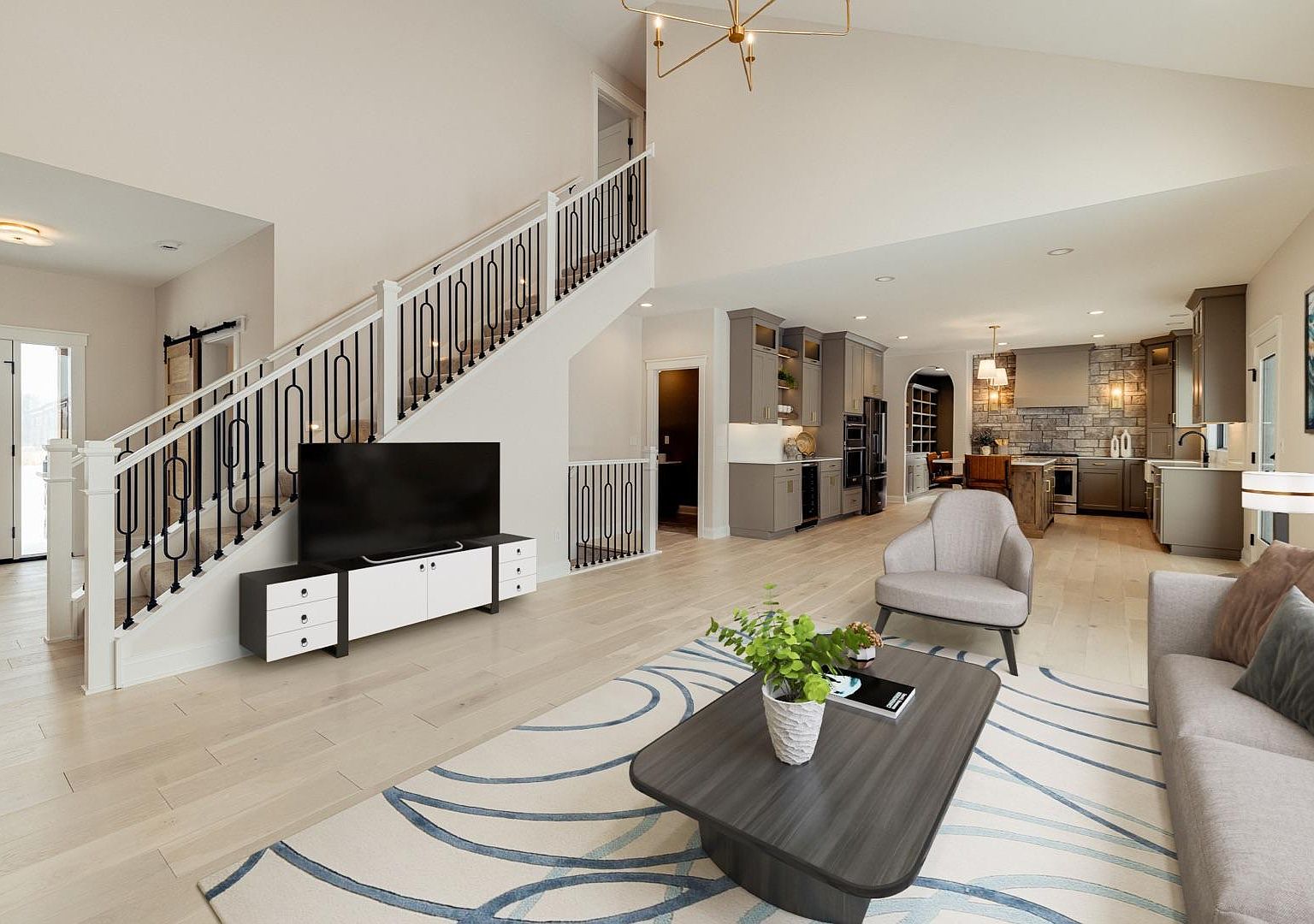The great room of 2762 Mayo Prairie Lane: a two-story vaulted ceiling, a knotty alder feature wall rising above a stacked-stone gas fireplace, brass chandelier, pale white oak floors, and a wall of prairie-view windows