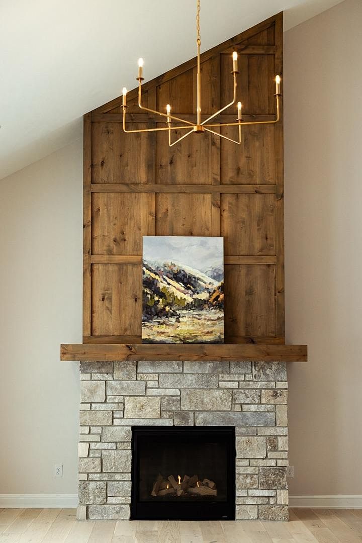 Close detail of the knotty alder fireplace tower at 2762 Mayo Prairie: paneled stained alder rising two stories to the vaulted ceiling, lit by a brass spider chandelier, with a stone hearth and reclaimed timber mantel below