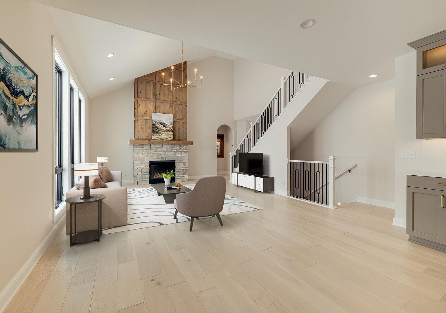 Wide view of the great room from the kitchen perspective at 2762 Mayo Prairie, showing the open staircase with iron balusters on the left, the vaulted alder feature wall on the right, and the lower-level walkout stair behind